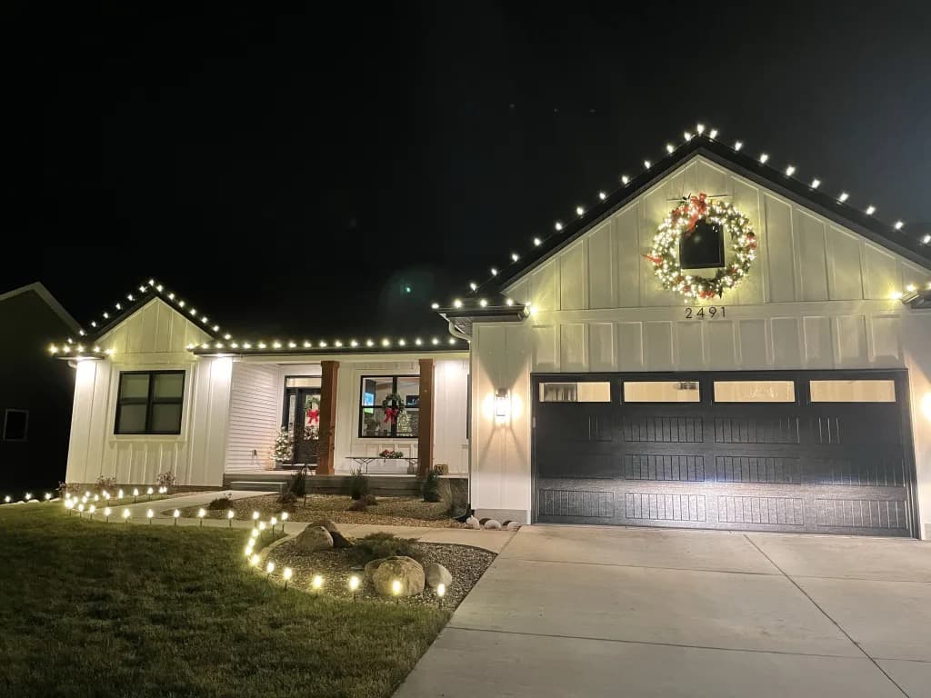 Two-story house at dusk with warm white Christmas lights outlining the roofline