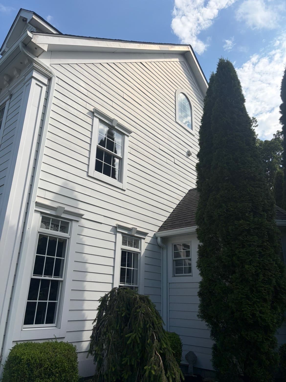 Two-story white siding, bright and algae-free after a soft wash, under a blue sky